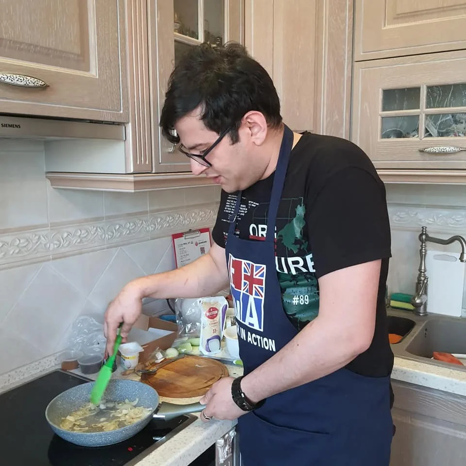 Ronnie cooking while wearing an English in Action apron